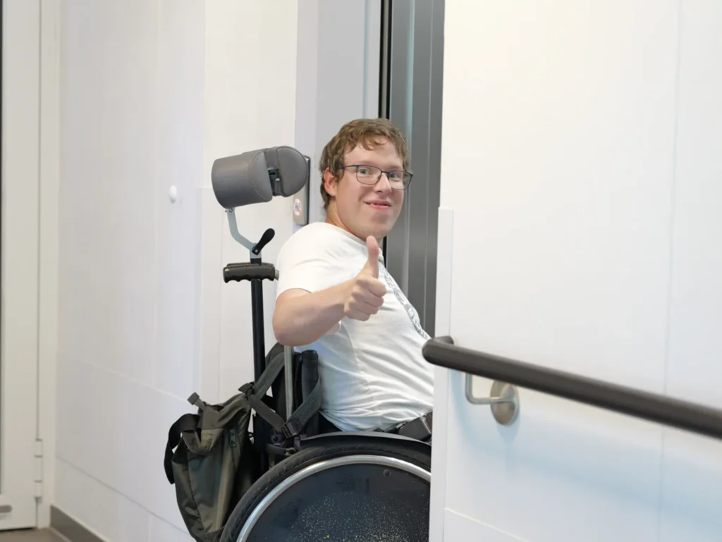 Erwachsene bei den Traumfängern. Ein erwachsener Mann sitzt im Rollstuhl und zeigt den Daumen nach oben.